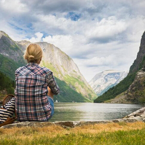A woman sitting peacefully on the bank of a serene fjord, reflecting on the beauty of nature.