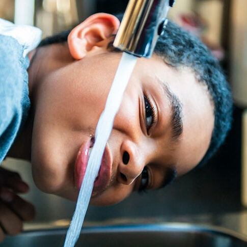 A child drinking water directly from a kitchen faucet, illustrating the importance of clean water access.
