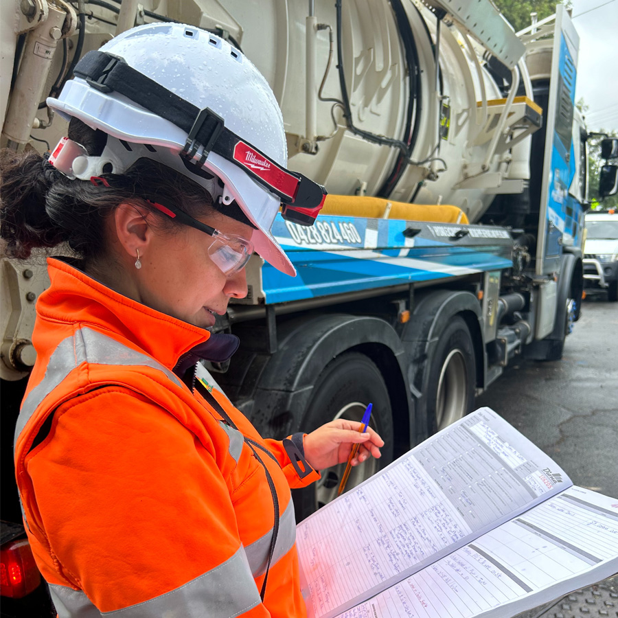 Female worker in high-vis gear reviewing a log book on site.